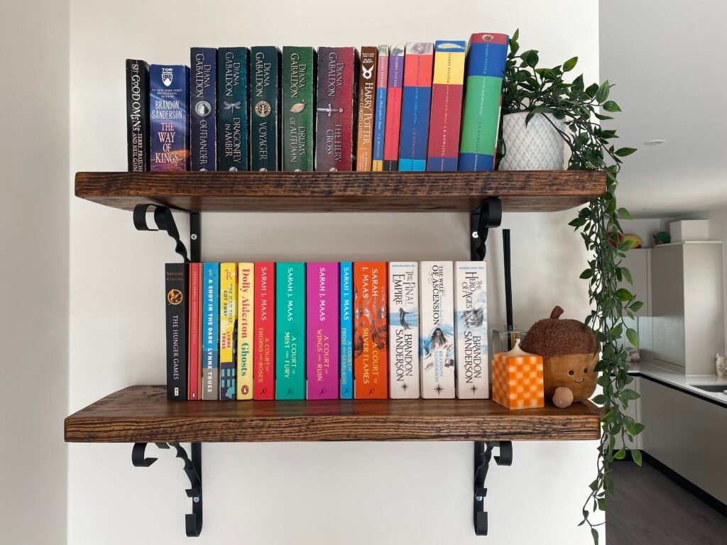 Two dark brown wooden book shelves that feature books and plants.